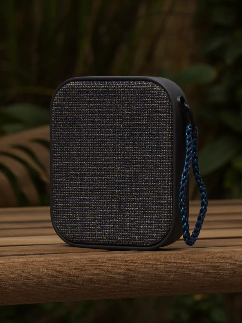 Kompakt Bluetooth-højttaler med vævet stofgrille på en træbænk udendørs